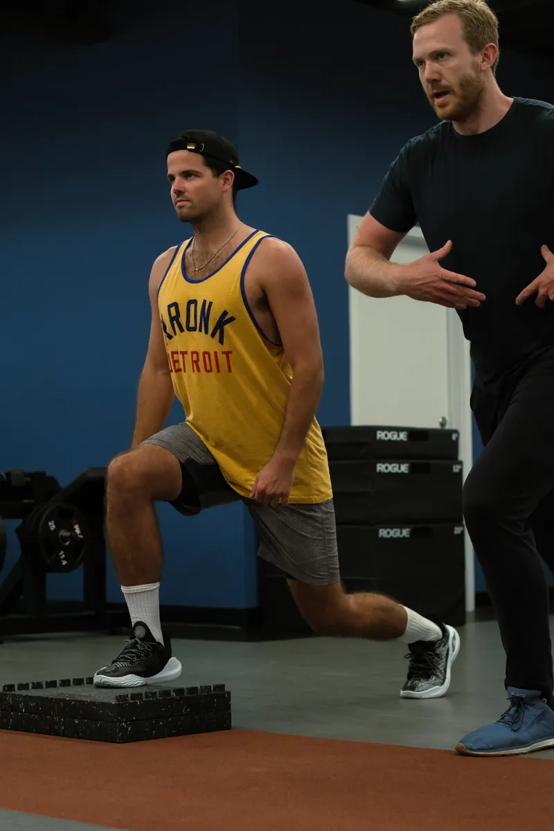A coach guides a client through walking lunges on the terracotta floor